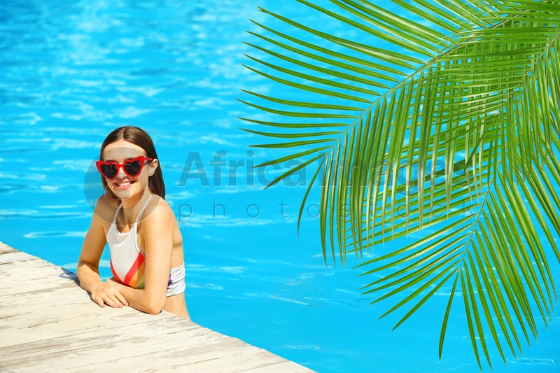 View of beautiful green tropical leaves and young woman in swimming pool on sunny day