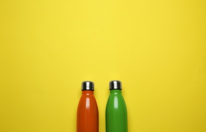 Modern thermo bottles on yellow background, flat lay. Space for text