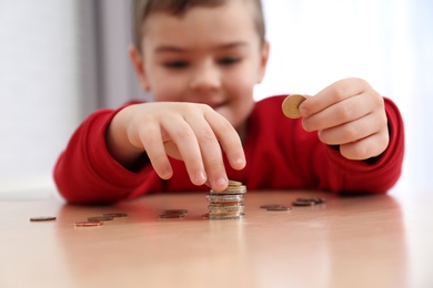 Photo of Cute little boy with coins at home, closeup. Counting money