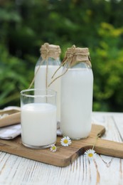 Tasty fresh milk and chamomile flowers on white wooden table outdoors