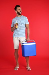 Happy man with cool box and bottle of beer on red background
