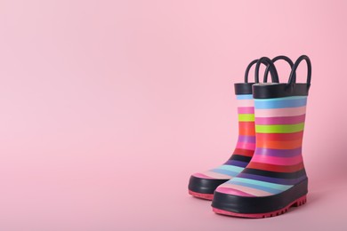 Pair of rainbow rubber boots on pink background. Space for text