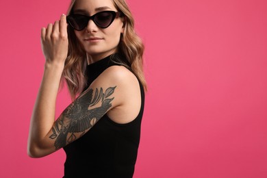 Beautiful woman with tattoos on arm against pink background. Space for text