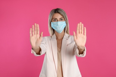 Woman in protective mask showing stop gesture on pink background. Prevent spreading of coronavirus
