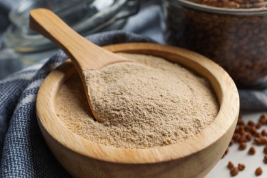 Buckwheat flour in bowl with wooden spoon on white table, closeup