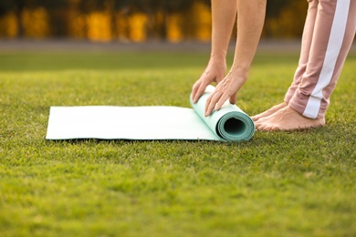 Mature woman unrolling yoga mat outdoors, closeup