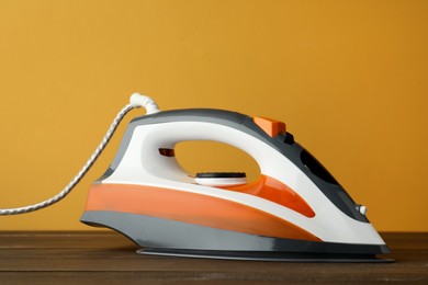 One modern iron on wooden table against orange background. Home appliance