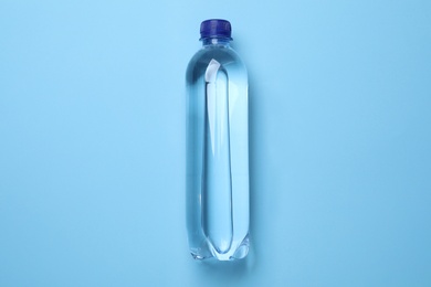 Plastic bottle with water on light blue background, top view