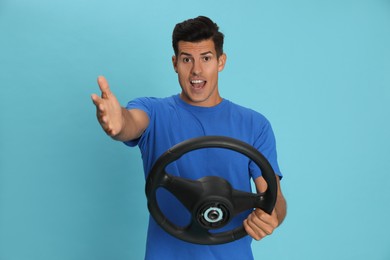 Emotional man with steering wheel on light blue background