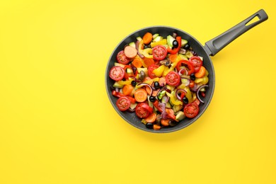 Mix of tasty vegetables in pan on yellow background, top view. Space for text