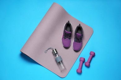 Exercise mat, dumbbells, bottle of water and shoes on turquoise background, flat lay