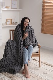 Young woman with chunky knit blanket in armchair at home