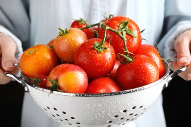 Woman holding colander with fresh ripe tomatoes on black background, closeup