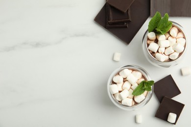 Glasses of delicious hot chocolate with marshmallows and fresh mint on white marble table, flat lay. Space for text