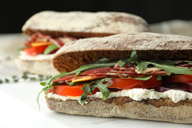 Delicious sandwiches with fresh vegetables and prosciutto on white table, closeup