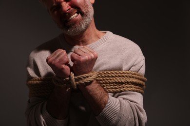 Photo of Emotional victim tied with rope on dark background, closeup. Hostage taking