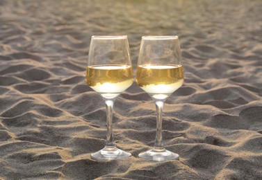 Photo of Glasses of tasty white wine on sand