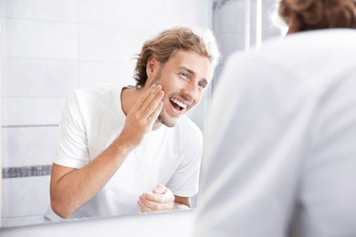 Young man washing face with soap near mirror in bathroom