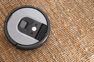 Modern robotic vacuum cleaner on brown rug, above view. Space for text