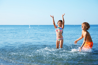 Cute little children having fun in sea on sunny day. Beach holiday