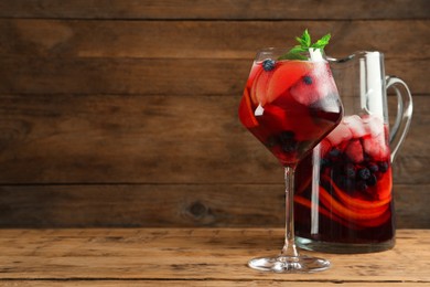 Glass and jug of Red Sangria with fruits on wooden table, space for text