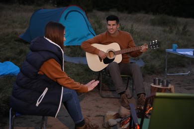 Couple with guitar sitting near bonfire at camping site