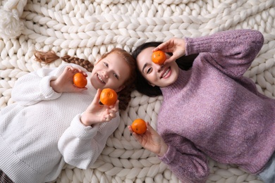 Happy girls with tangerines lying on knitted plaid, top view