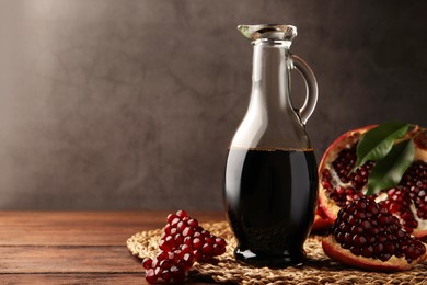 Photo of Glass jug of tasty pomegranate sauce and fresh ripe fruit on wooden table. Space for text