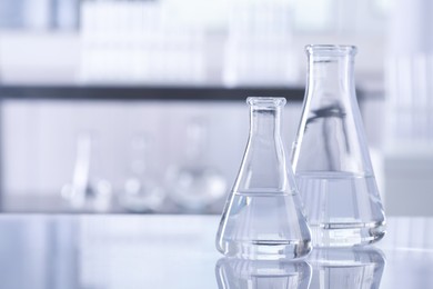 Conical flasks with transparent liquid on table in laboratory. Space for text