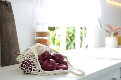 Photo of Red onions in mesh tote bag on countertop of kitchen