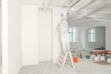 Decorator in uniform painting wall with sprayer indoors, back view