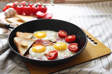 Delicious fried eggs with bacon and tomatoes in pan on table
