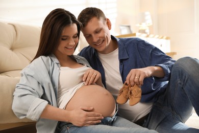 Young pregnant woman and her husband with baby's shoes at home