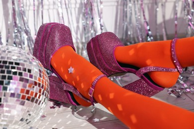 Photo of Woman in orange tights and pink high heeled shoes near disco ball indoors, closeup