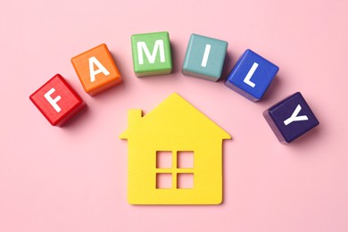 House figure and word Family made of colorful cubes with letters on pink table, flat lay