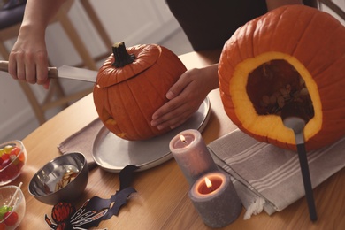 Woman making pumpkin jack o'lantern at wooden table, closeup. Halloween celebration