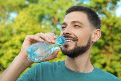 Photo of Happy man drinking water outdoors on hot summer day. Refreshing drink