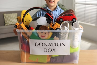 Little boy holding donation box with goods and toys at home, closeup