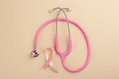 Pink ribbon and stethoscope on beige background, flat lay. Breast cancer concept