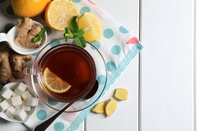 Photo of Cup of delicious ginger tea, sugar cubes and lemons on white wooden table, flat lay. Space for text