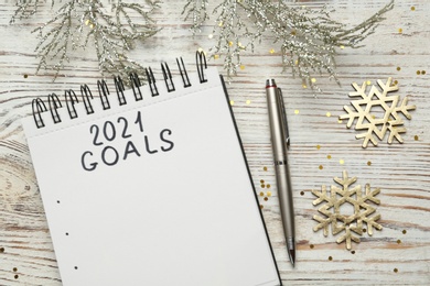 Inscription 2021 Goals in notebook, new year aims. Christmas decor and stationery on white wooden background, flat lay