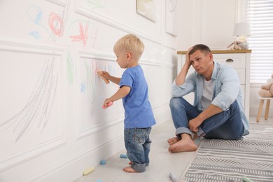 Upset father watching his little son drawing on wall at home