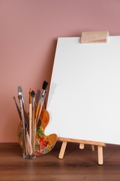 Easel with empty canvas and art supplies on wooden table