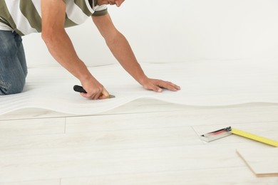 Photo of Professional worker cutting polyethylene foam during installation of laminate flooring indoors, closeup