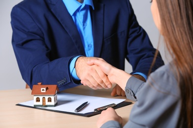 Woman shaking hands with real estate agent at table in office, closeup. Home insurance