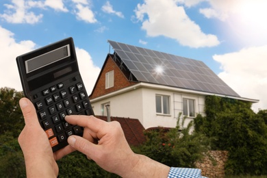 Man using calculator against house with installed solar panels. Renewable energy and money saving