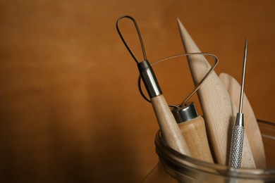 Photo of Set of clay modeling tools in glass jar on brown background, closeup. Space for text