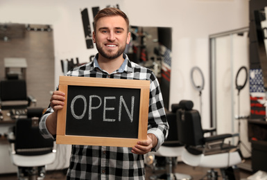 Young business owner holding OPEN sign in his barber shop