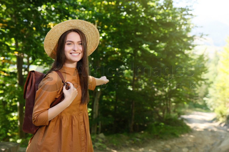 Happy woman with backpack and hat enjoying her walk in forest