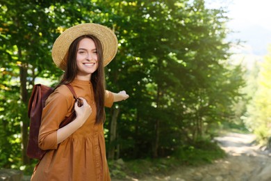 Happy woman with backpack and hat enjoying her walk in forest